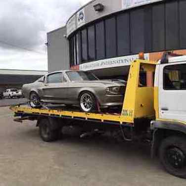A new grey Ford Mustang on the back of a flat deck tow truck