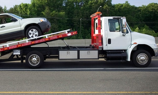 A flat bed tow truck loading a vehicle from the side of the highway