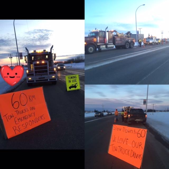 A bunch of tow trucks parked on the side of the highway with homemade signs asking people to slow down to 6o KMS while passing.