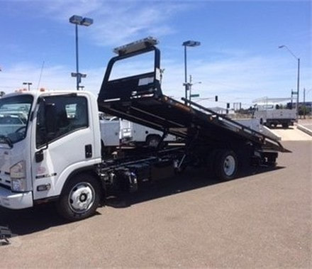 A new flat deck tow truck with is ramp tilted back in a car dealership parking lot