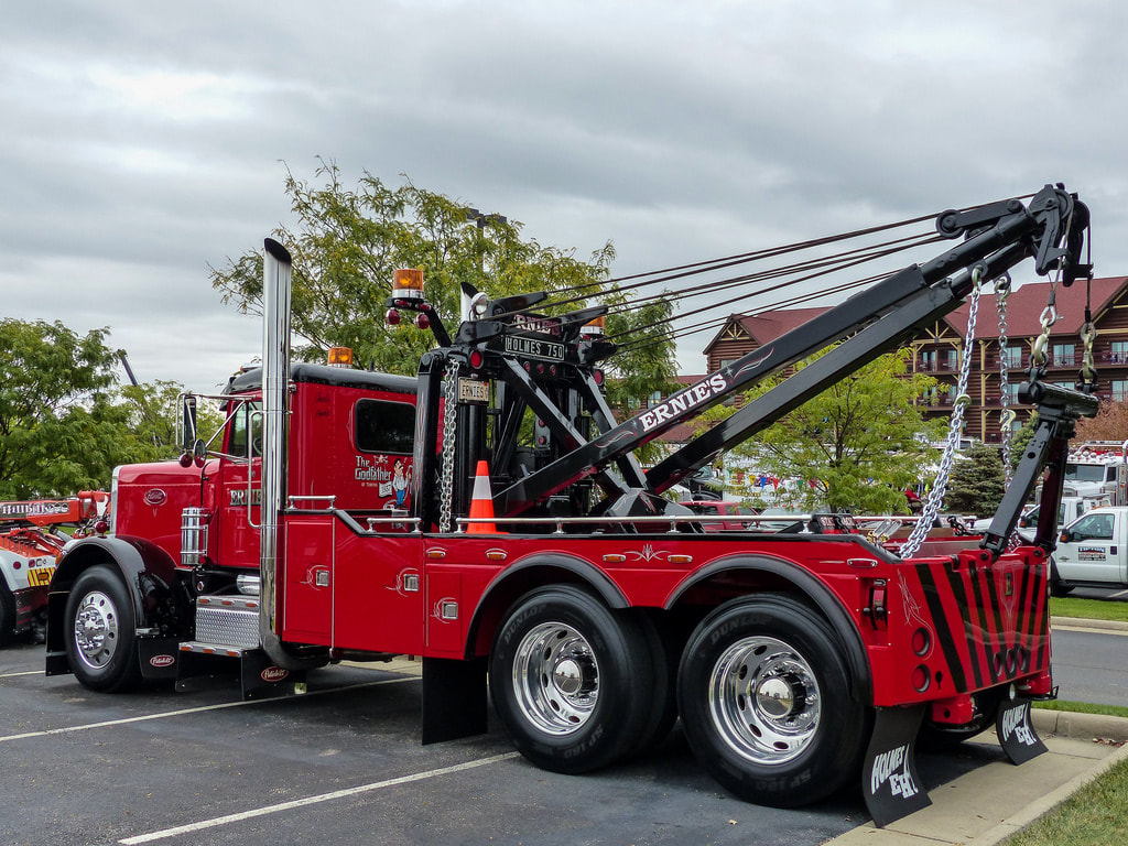 A large Red Peterbilt truck with heavy duty boom arms and winches on the back