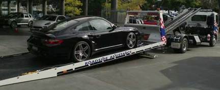 A black porche 911 being loaded on to the back of a flat deck tow truck