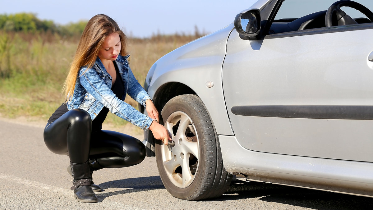 A young lady fixing her tire on her car