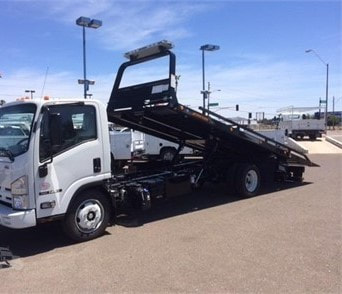 A medium duty lat bed truck with the bed tilted up, ready to pick up a vehicle.