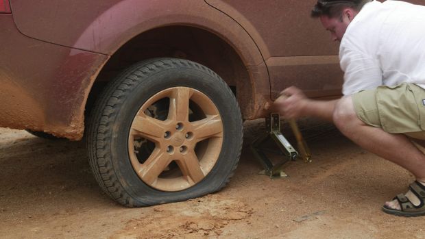 A man replacing the flat tire on his vehicle in the dirt