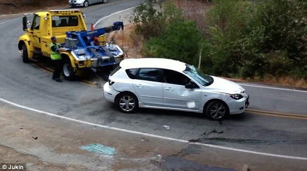 A yellow tow truck recovering a car on a bend in the road after an accident